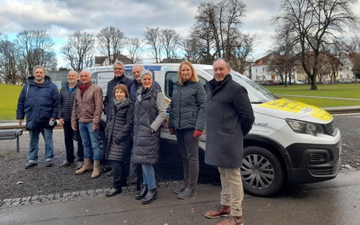 Gruppenbild mit einigen Ehrenamtlichen, die das im Hintergrund zu sehende Fahrzeug steuern.