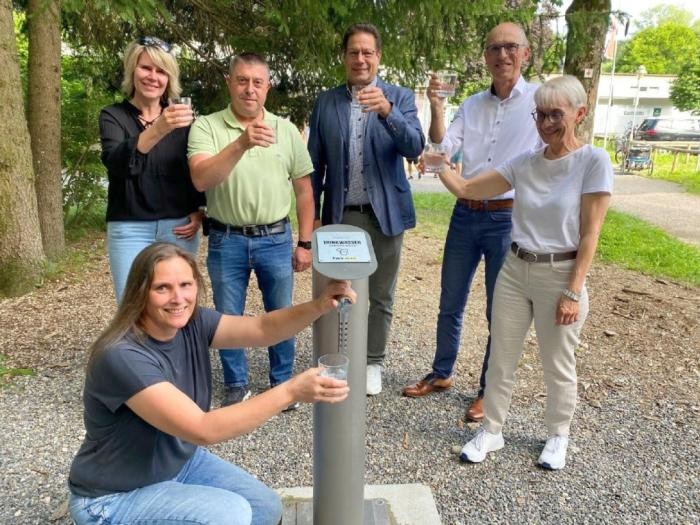 Gruppenbild: Sechs Vertreterinnen und Vertreter von Stadt, TWS und Bürgerstiftung testen das Wasser aus dem neuen Trinkwasserspender am Freibad 