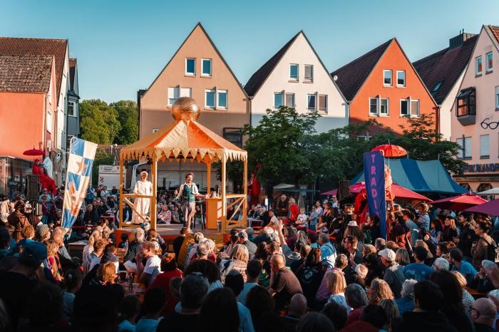 Auf einer Bühne mitten in der Stadt spielen Schauspieler Bauernkriegsszenen. Sehr viele Menschen schauen zu