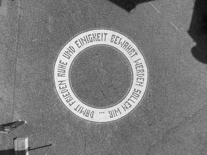 Eine in den gepflasterten Boden eingelassene, kreisrunde Schrift